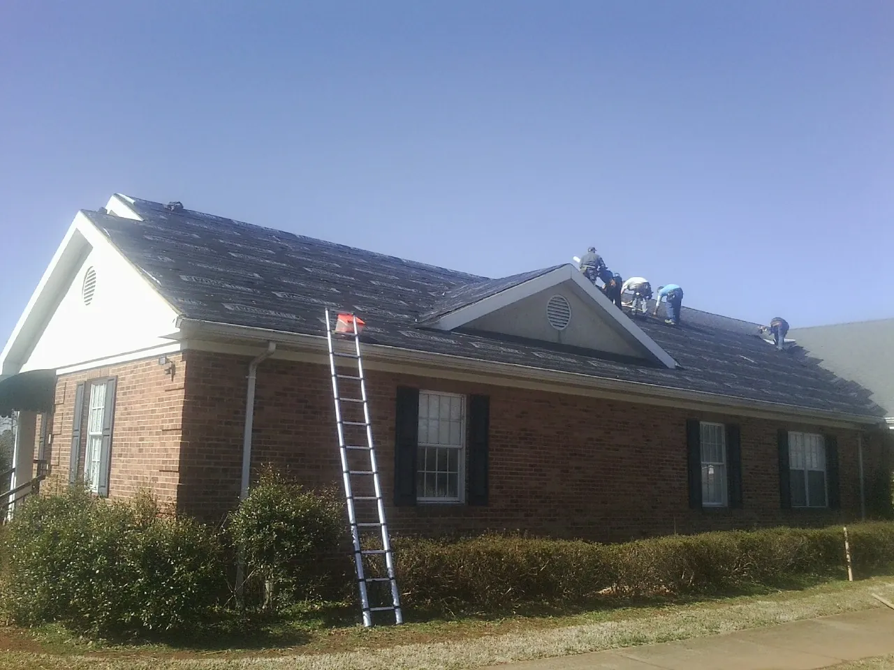 Crew tearing shingles off a brick ranch roof with a ladder set — Metal Roof Repair work by our crew in Wilson