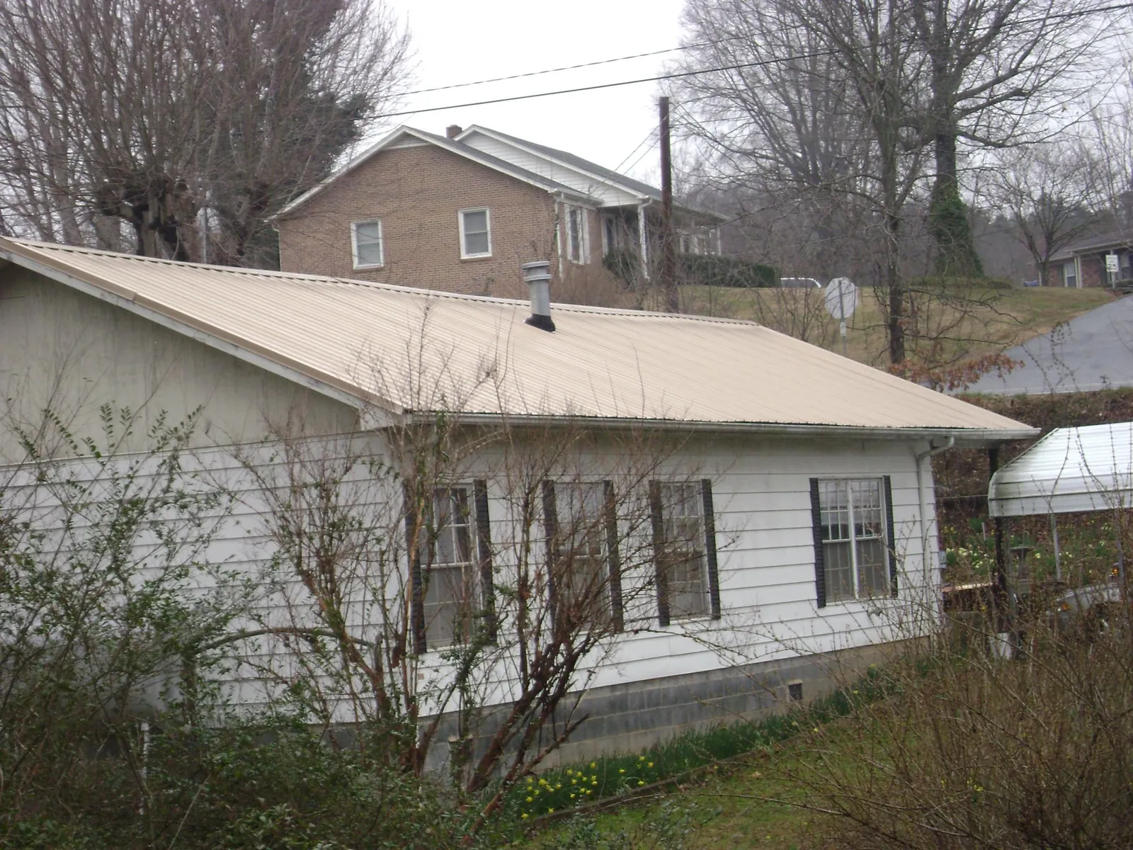 Tan metal roof on a white sided house set into a hillside — Commercial Roofing by Roofing Brothers in Wilson