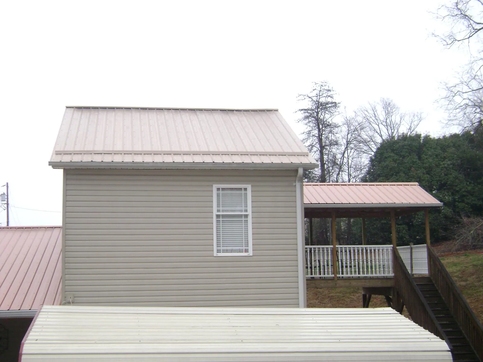 Tan metal roofs on a two story addition and attached porch, from a Roof Replacement job in Wilson